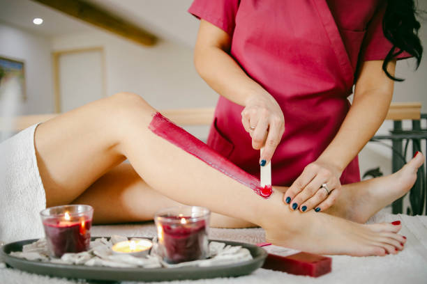 A beautician waxes a woman's leg in a salon